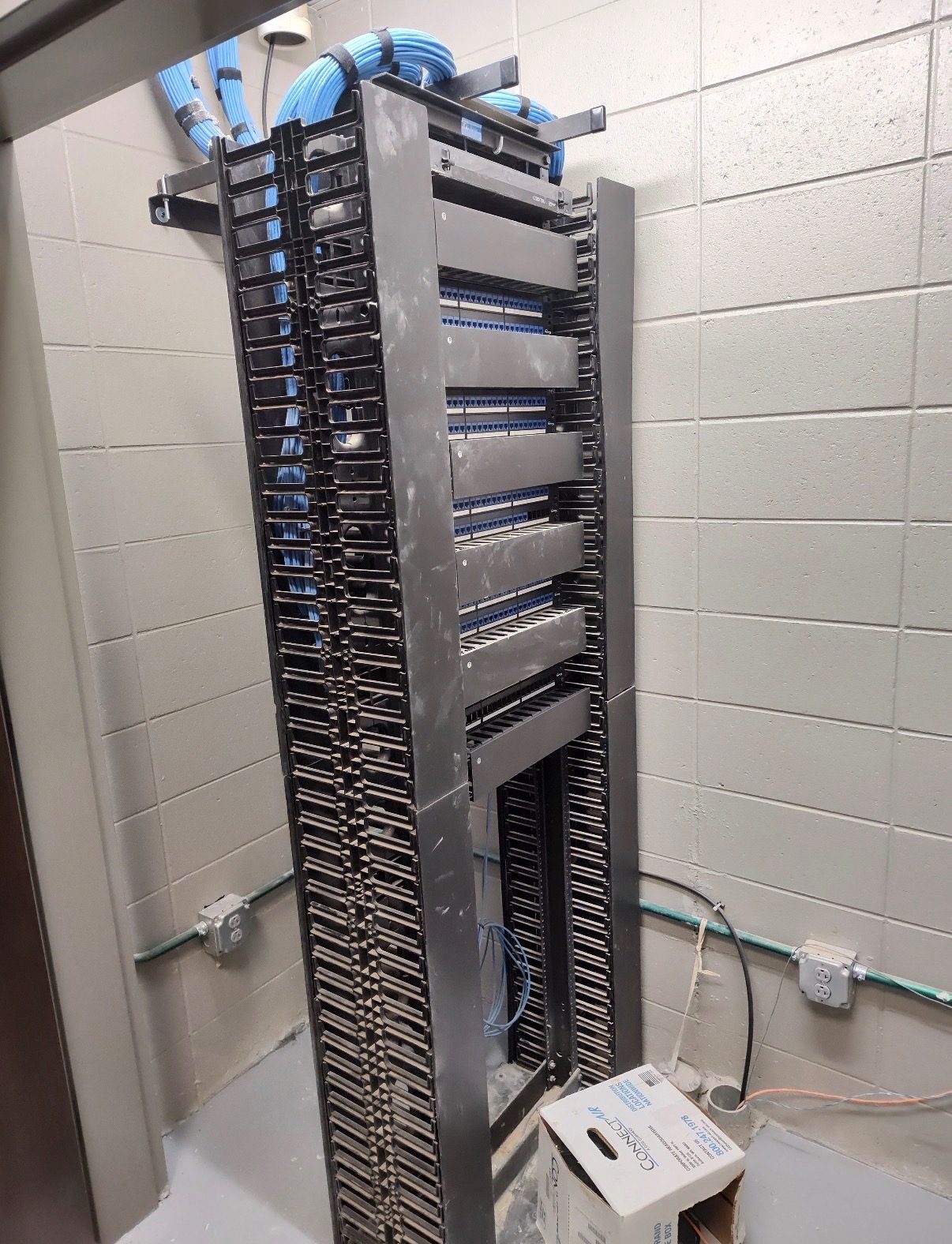 Two-post rack with vertical cable management and blue Cat6 landing on patch panels in a new telecom room
